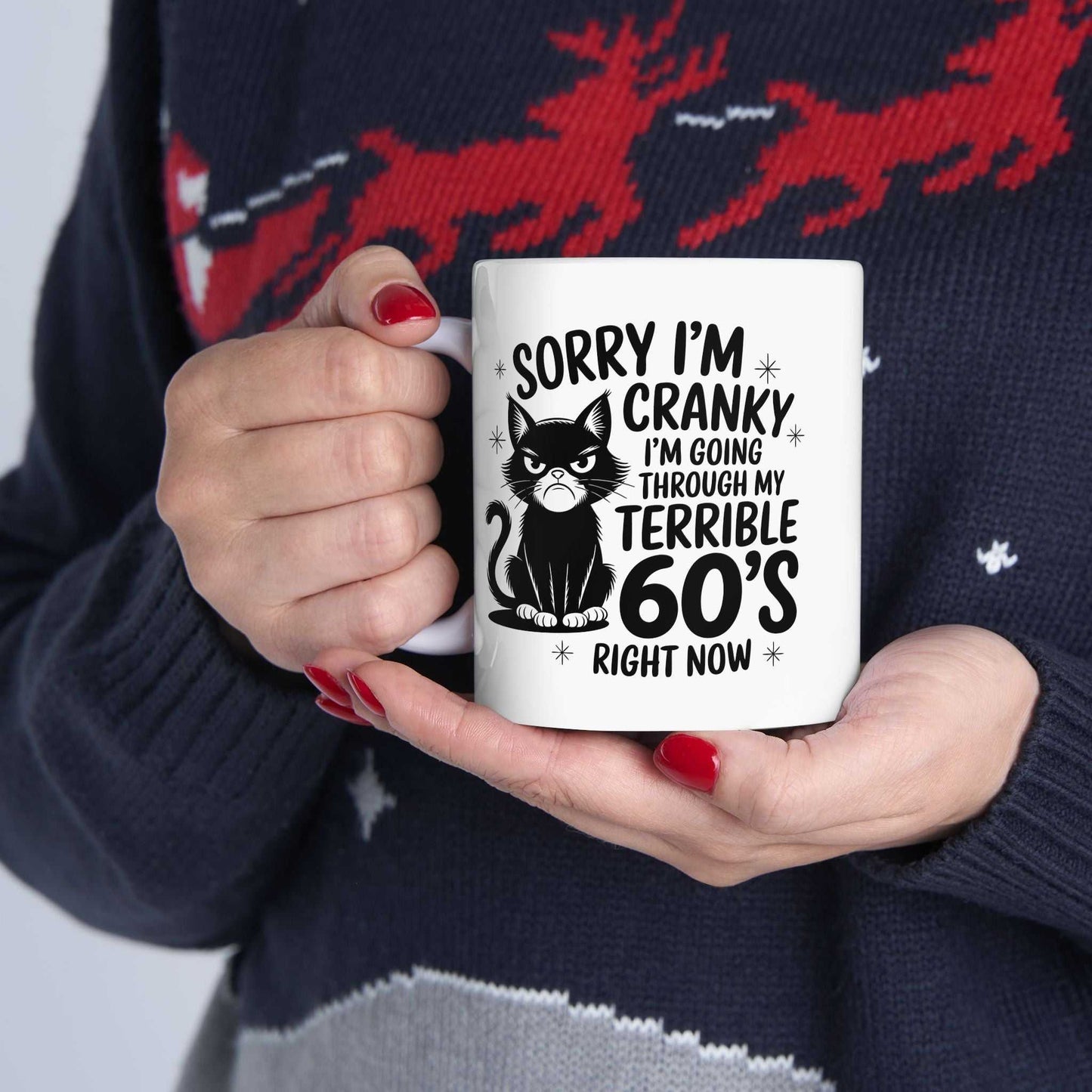 Person holding a mug with a humorous design and text, wearing a festive sweater.