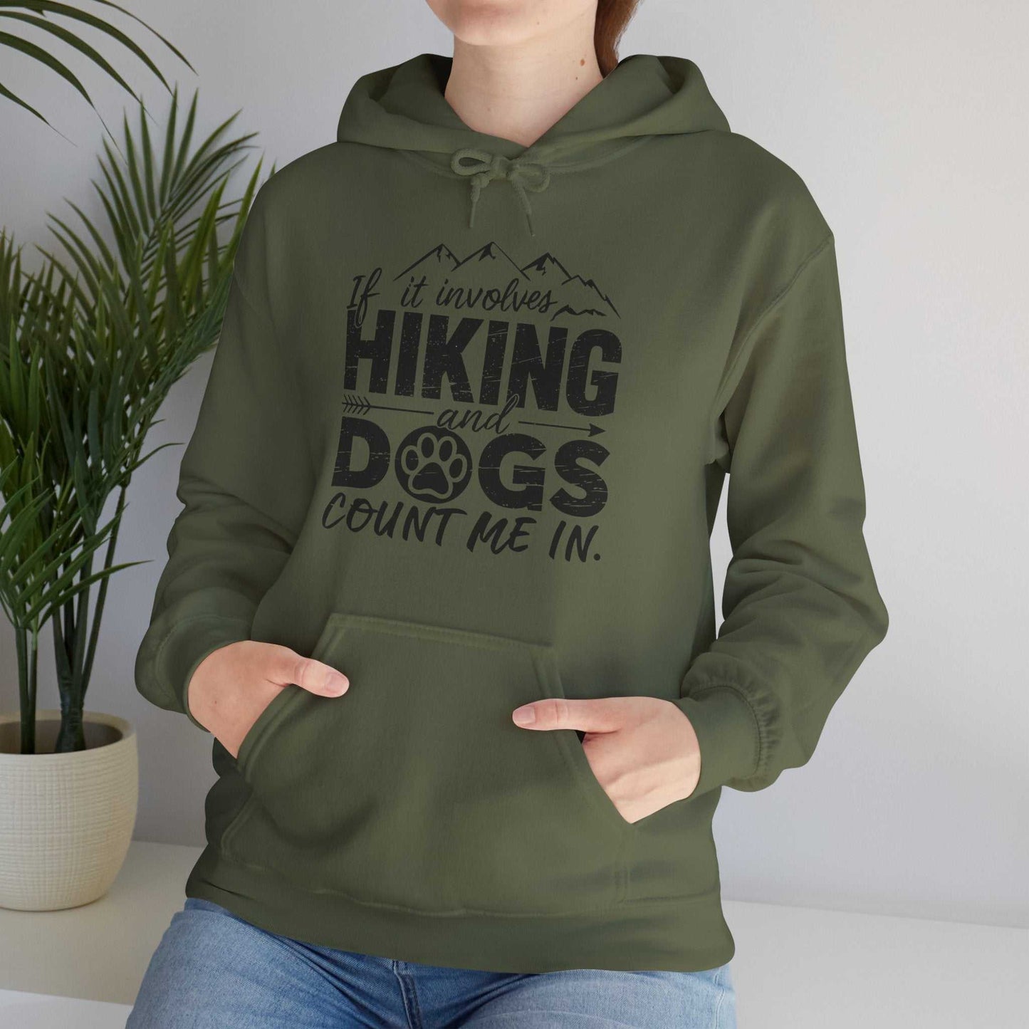 Person wearing a green hoodie with text 'If it involves hiking and dogs, count me in.' in a home setting.