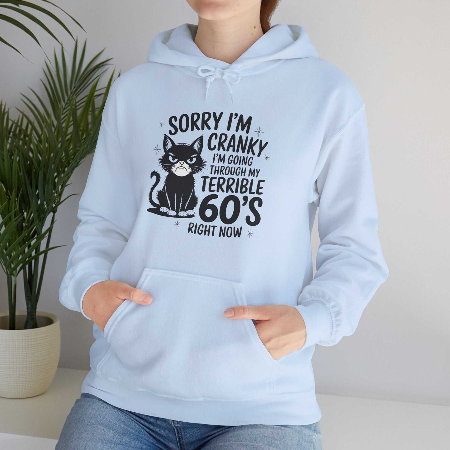 Light blue hoodie with a graphic of a cat and text, worn by a person, against a neutral background.