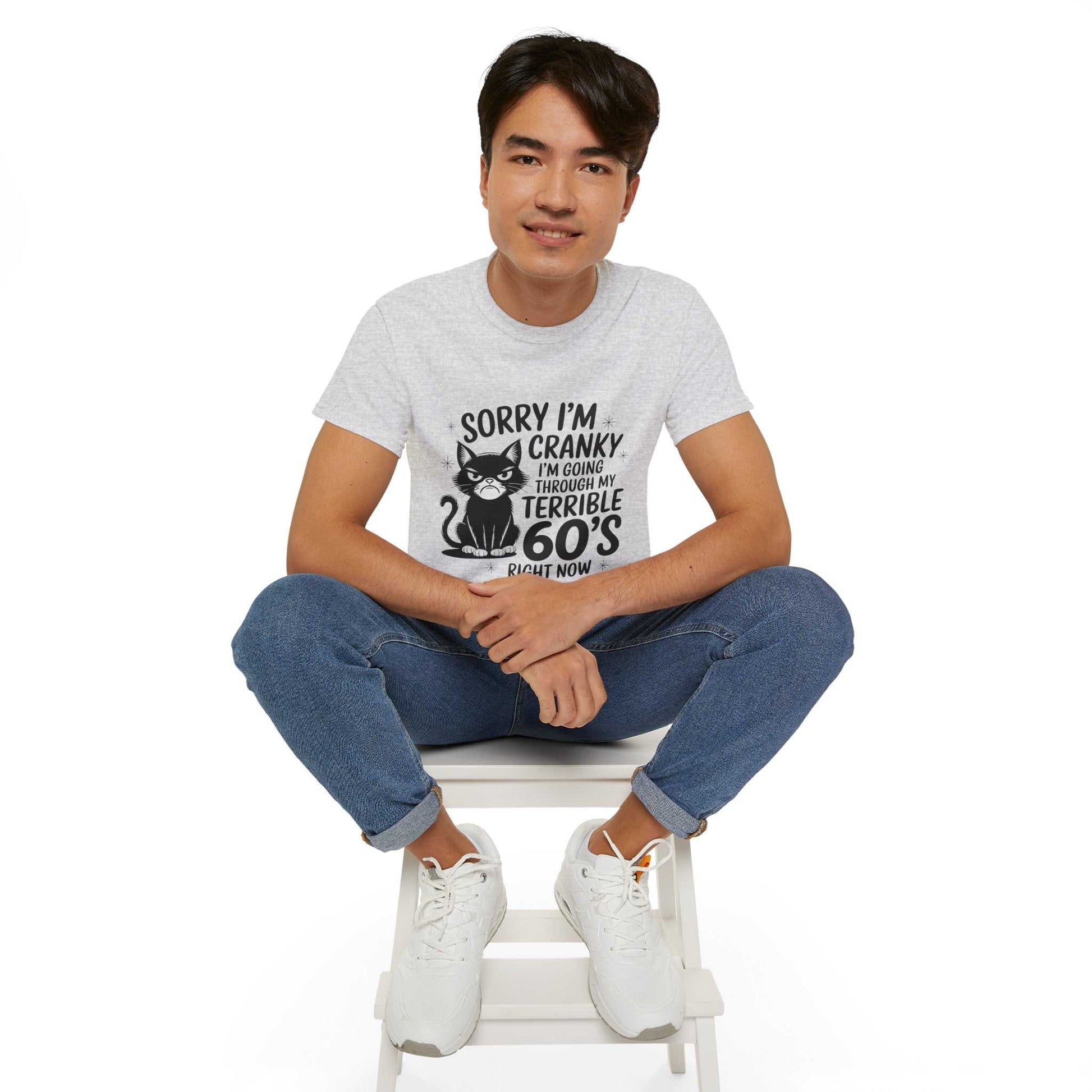 Person wearing a t-shirt with a graphic and text, sitting on a white stool against a white background