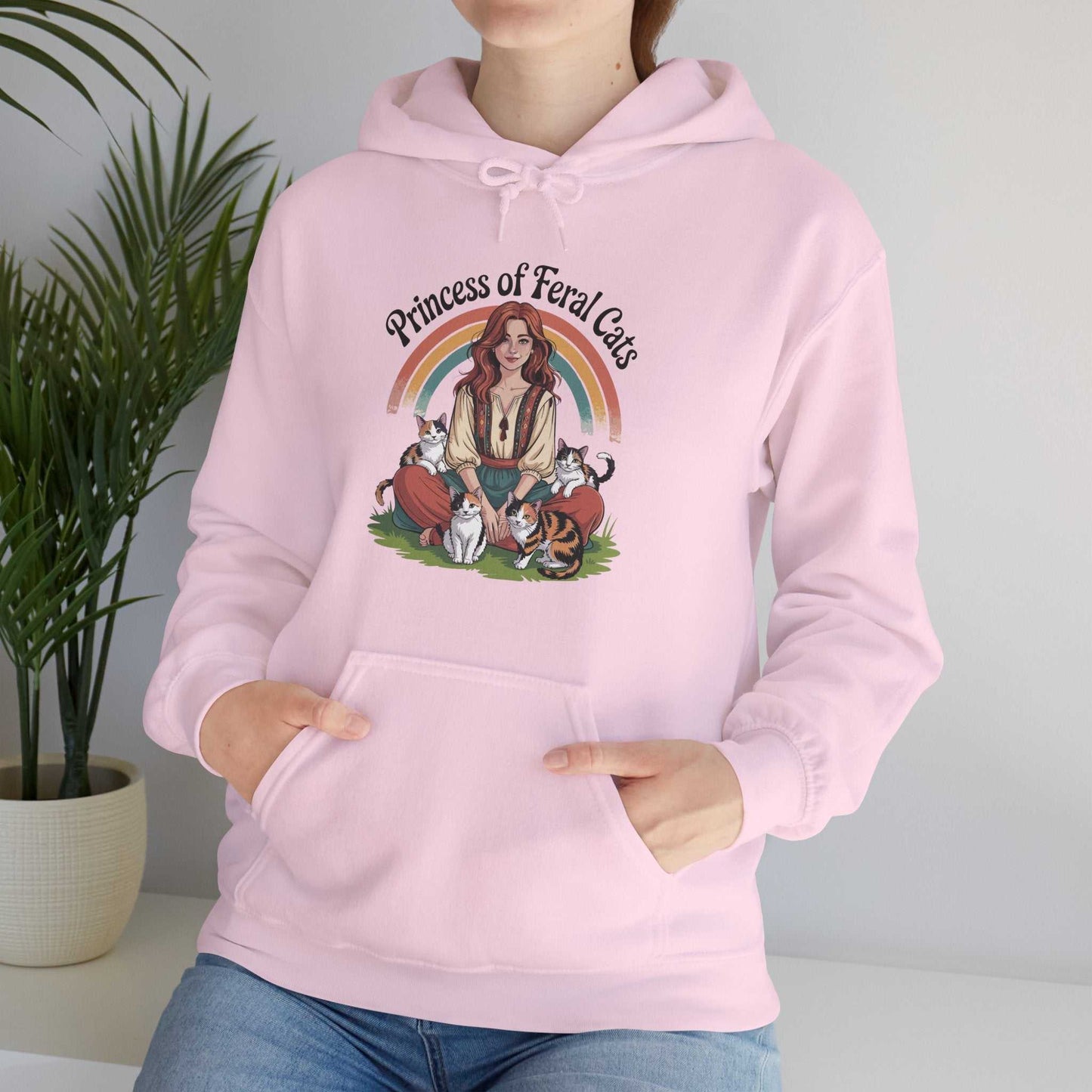 Person wearing a pink hoodie with 'Princess of Feral Cats' design, standing next to a plant.