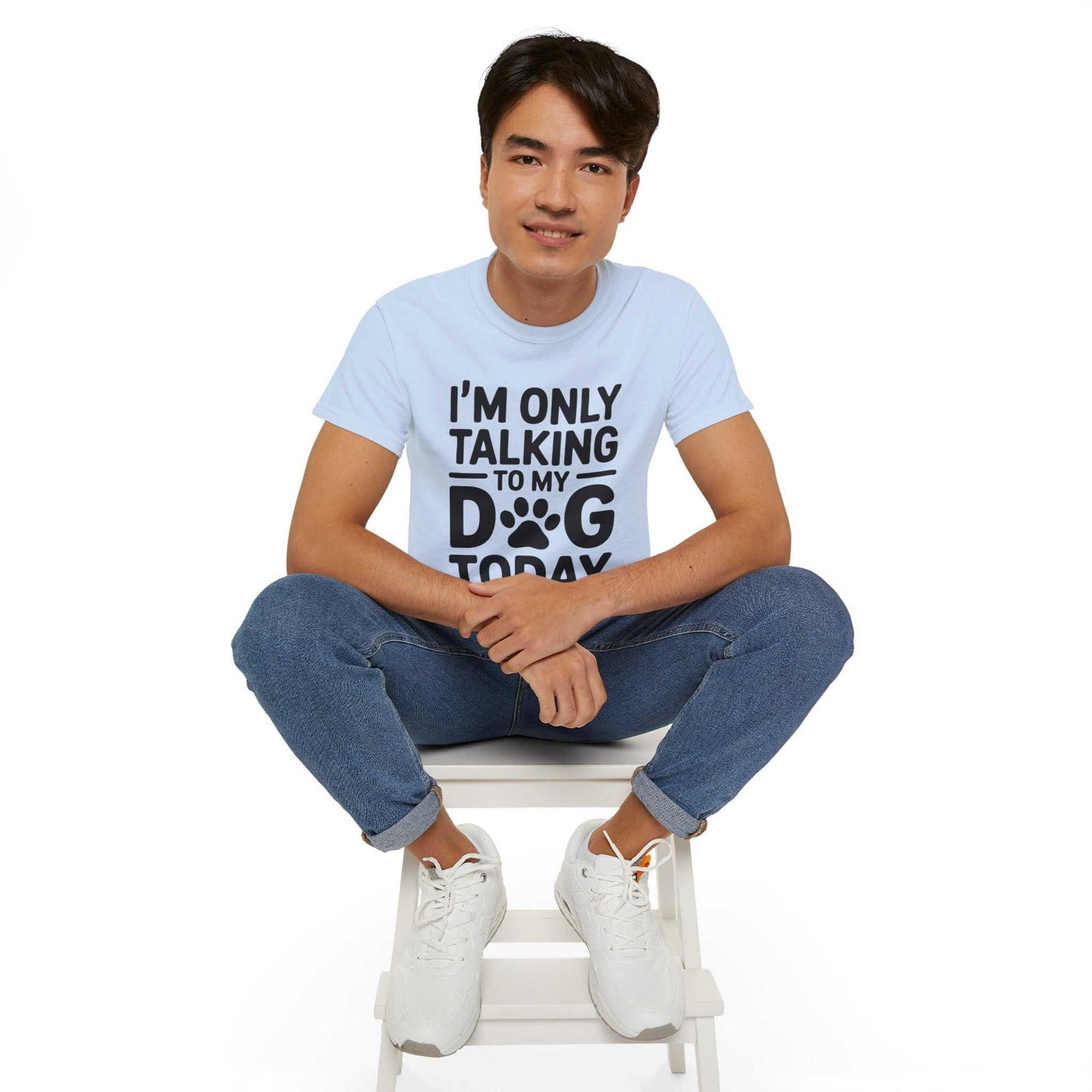 Person wearing a light blue t-shirt with text sitting on a white stool against a white background