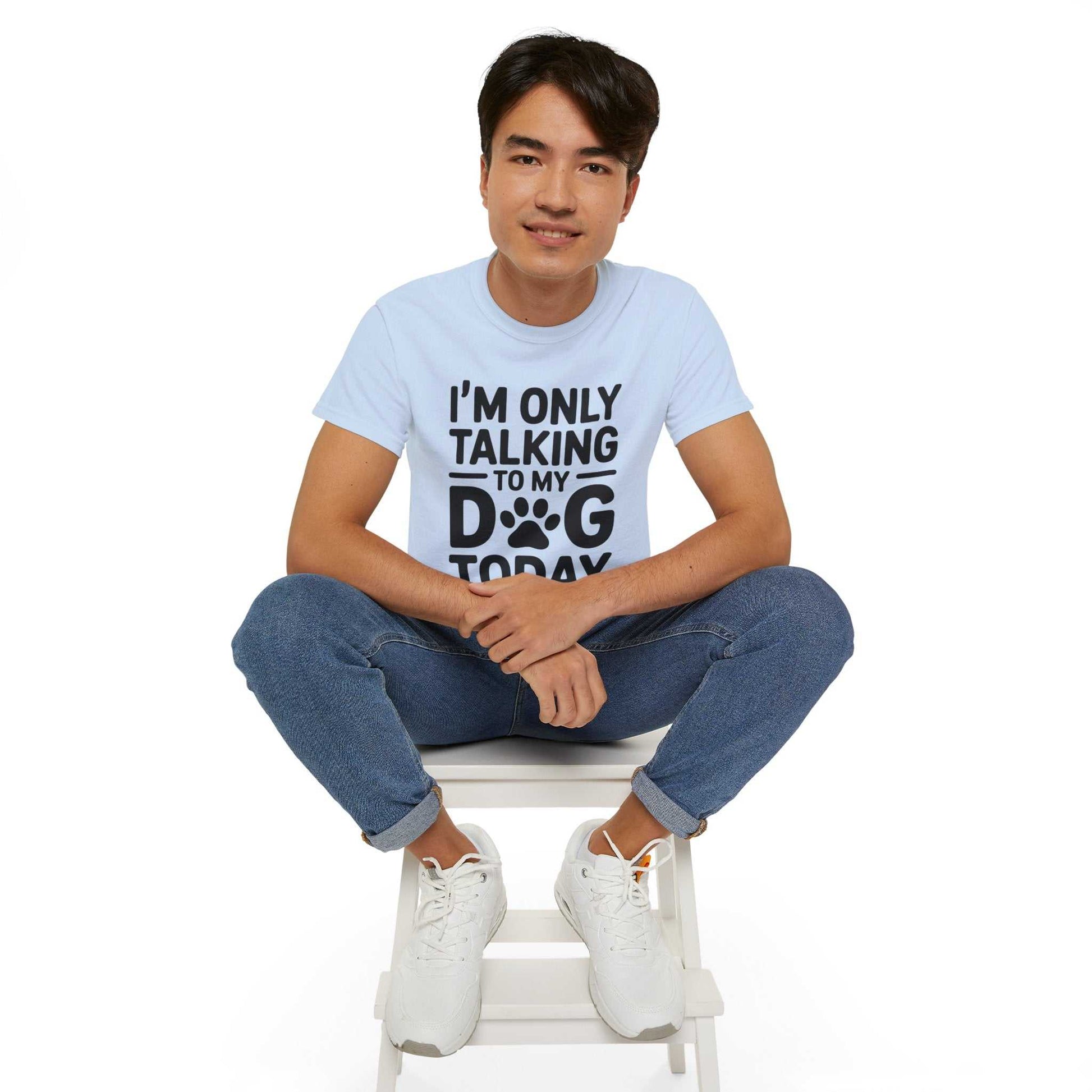 Person wearing a light blue t-shirt with text sitting on a white stool against a white background