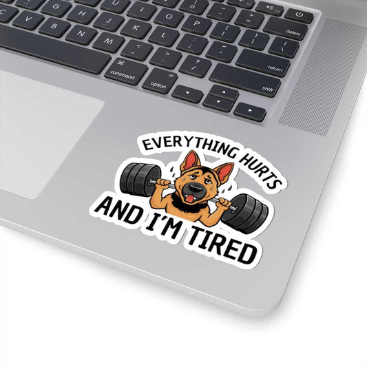 Laptop with a sticker of a dog lifting weights and text 'Everything hurts and I'm tired' on a white background