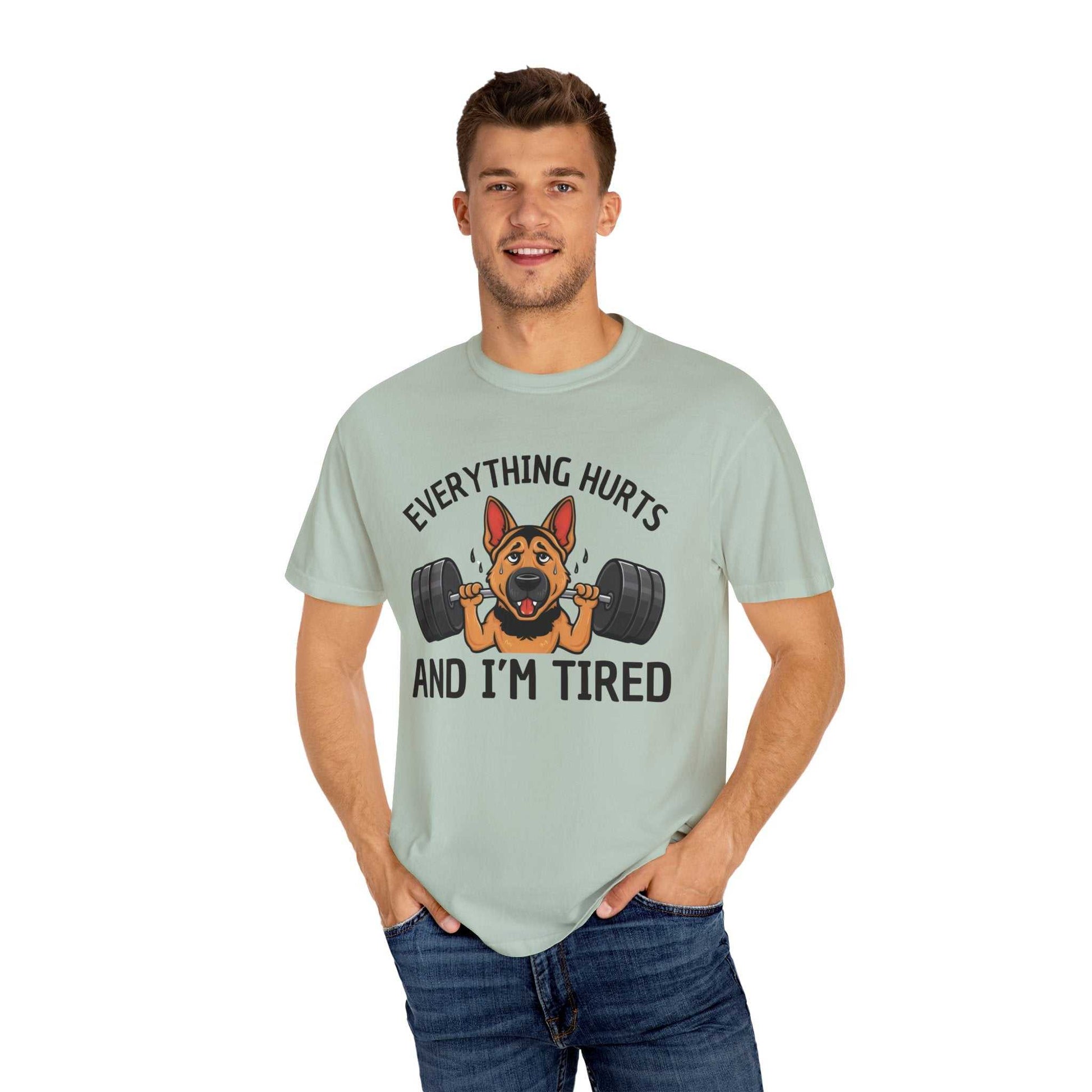 Man wearing a light green t-shirt with a graphic of a dog lifting weights and text 'EVERYTHING HURTS AND I'M TIRED' on a white background.