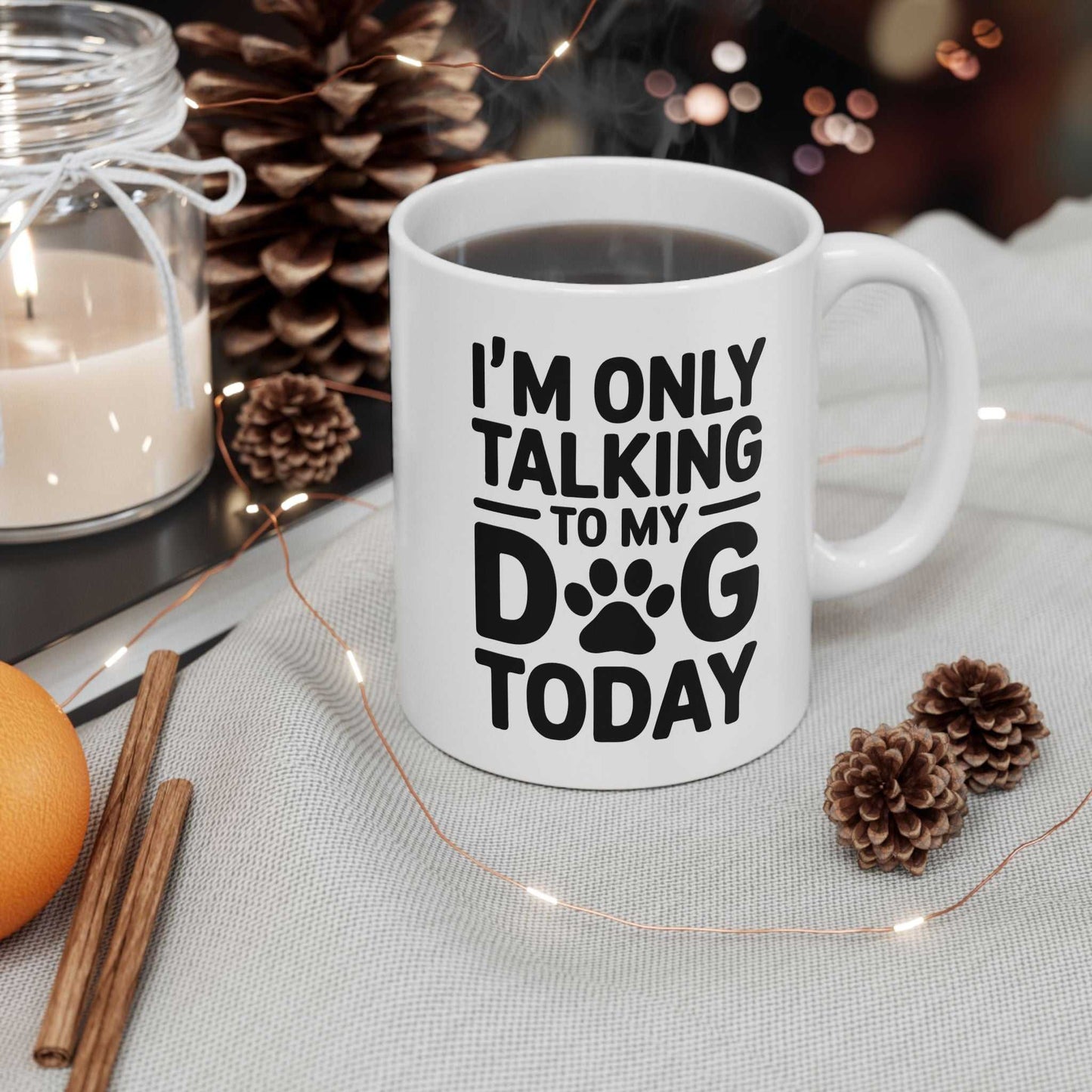 White mug with 'I'm only talking to my dog today' text on a table with decorative items.