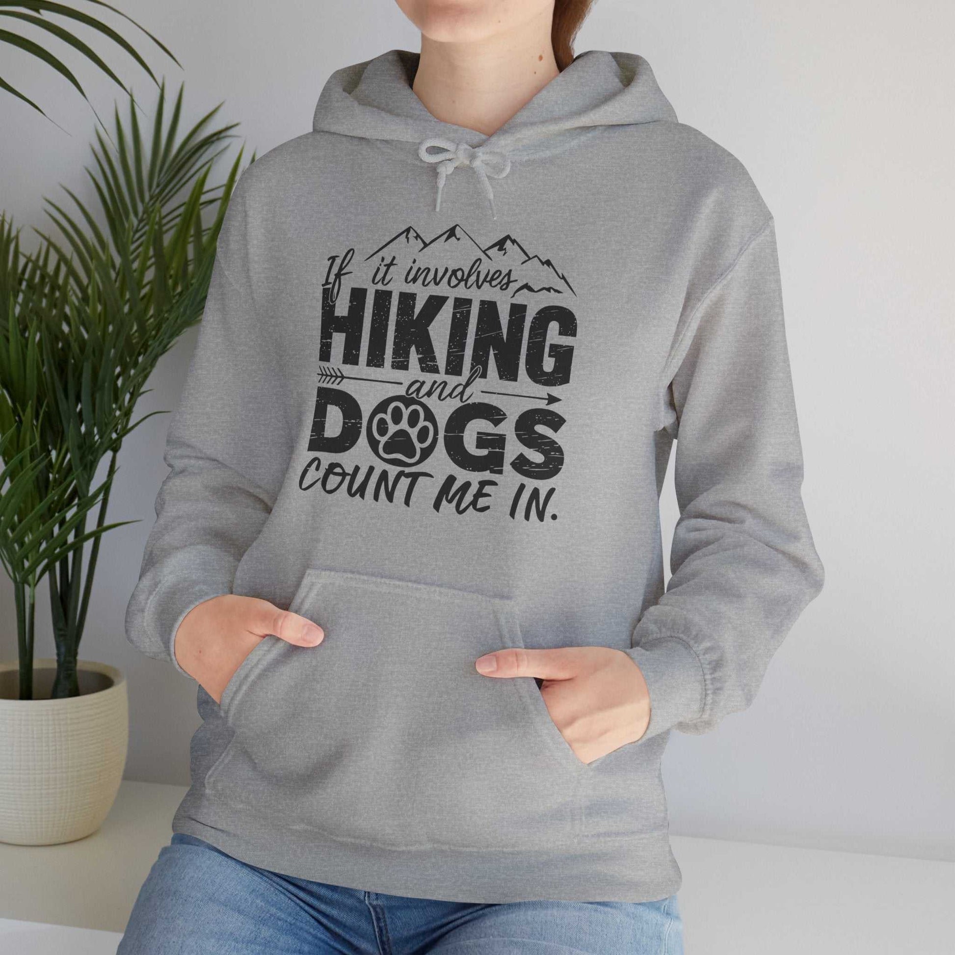 Person wearing a gray hoodie with a hiking and dogs design, standing indoors with a plant in the background.