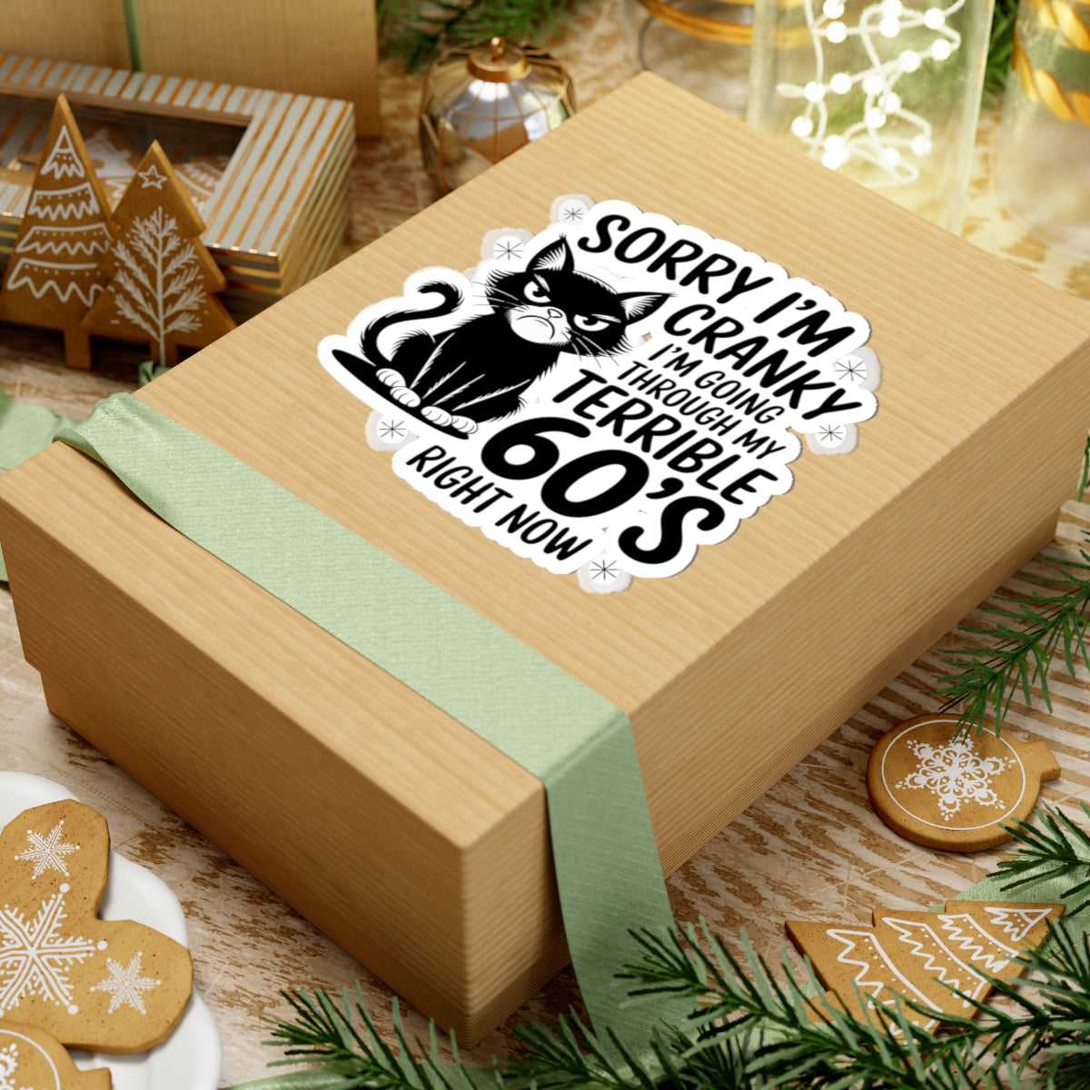 Gift box with a humorous cat sticker on a festive background with cookies and decorations.