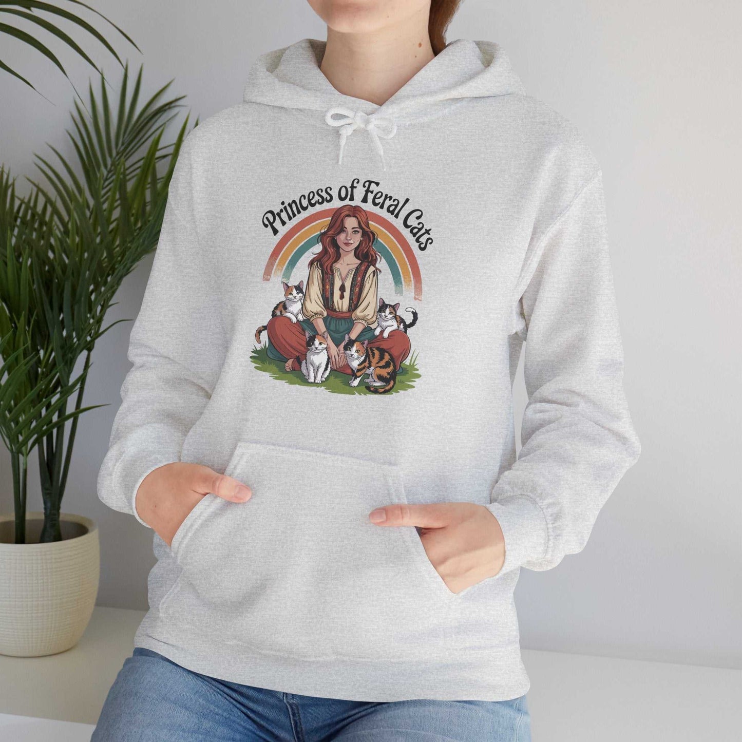 Person wearing a gray hoodie with a graphic design of a woman and cats, labeled 'Princess of Feral Cats', in a room with a plant.