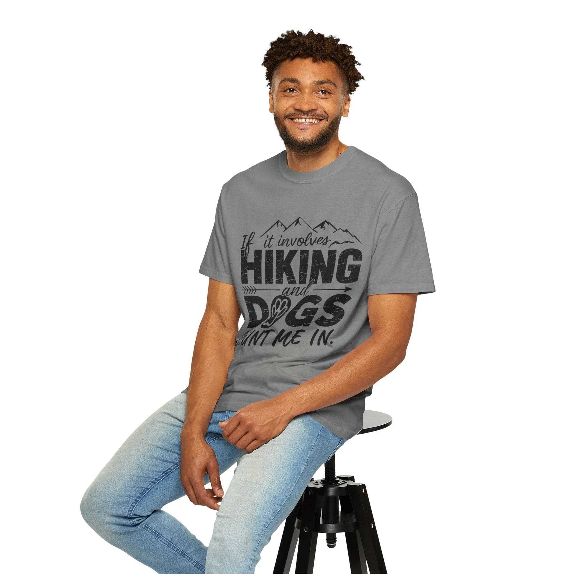 Man wearing a gray t-shirt with 'Hiking and Dogs' text, sitting on a stool against a white background