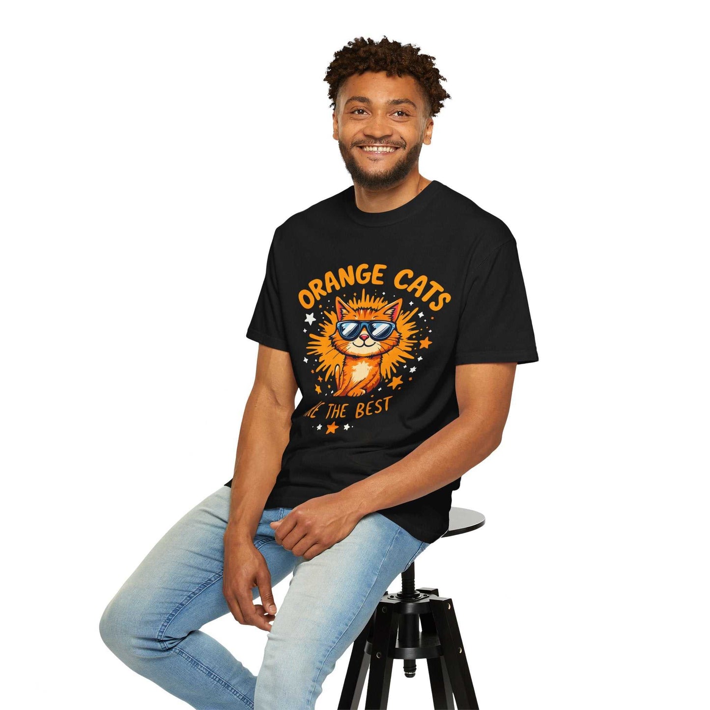 Man wearing a black t-shirt with a cat graphic and text, sitting on a stool against a white background