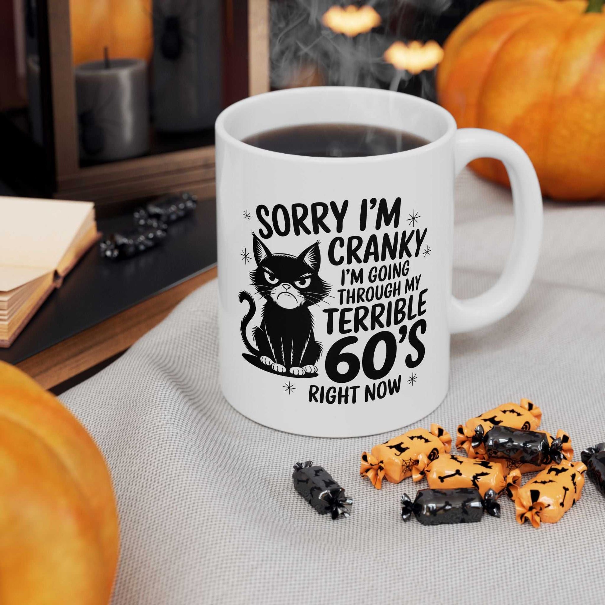 Mug with Halloween-themed text and cat illustration on a table with pumpkins and treats.