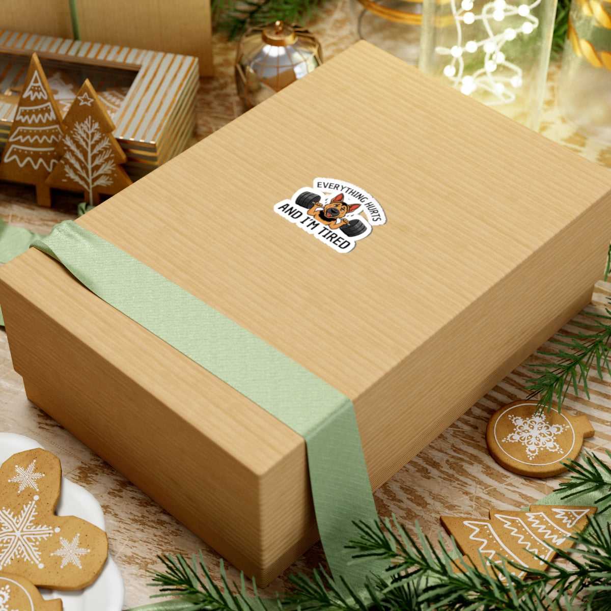 Gift box with a green ribbon and a sticker on a festive background with cookies and lights.