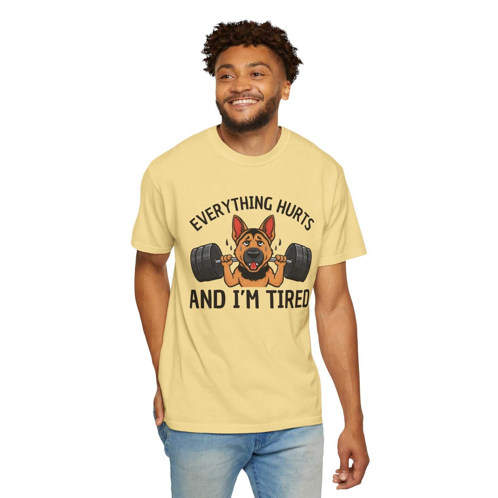 Man wearing a yellow t-shirt with a graphic of a dog lifting weights and text 'Everything hurts and I'm tired' on a white background.