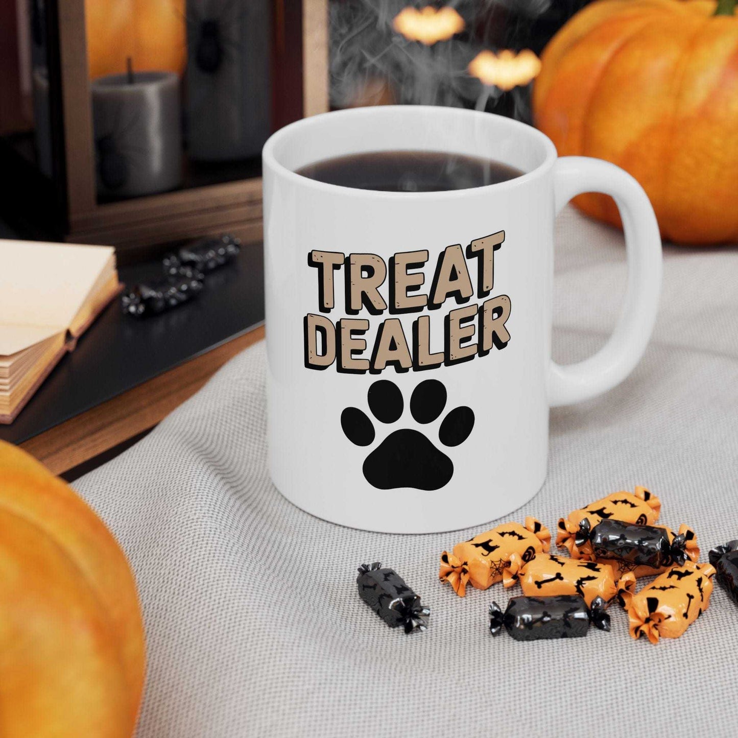 Mug with 'Treat Dealer' text and paw print, surrounded by Halloween-themed treats on a table.