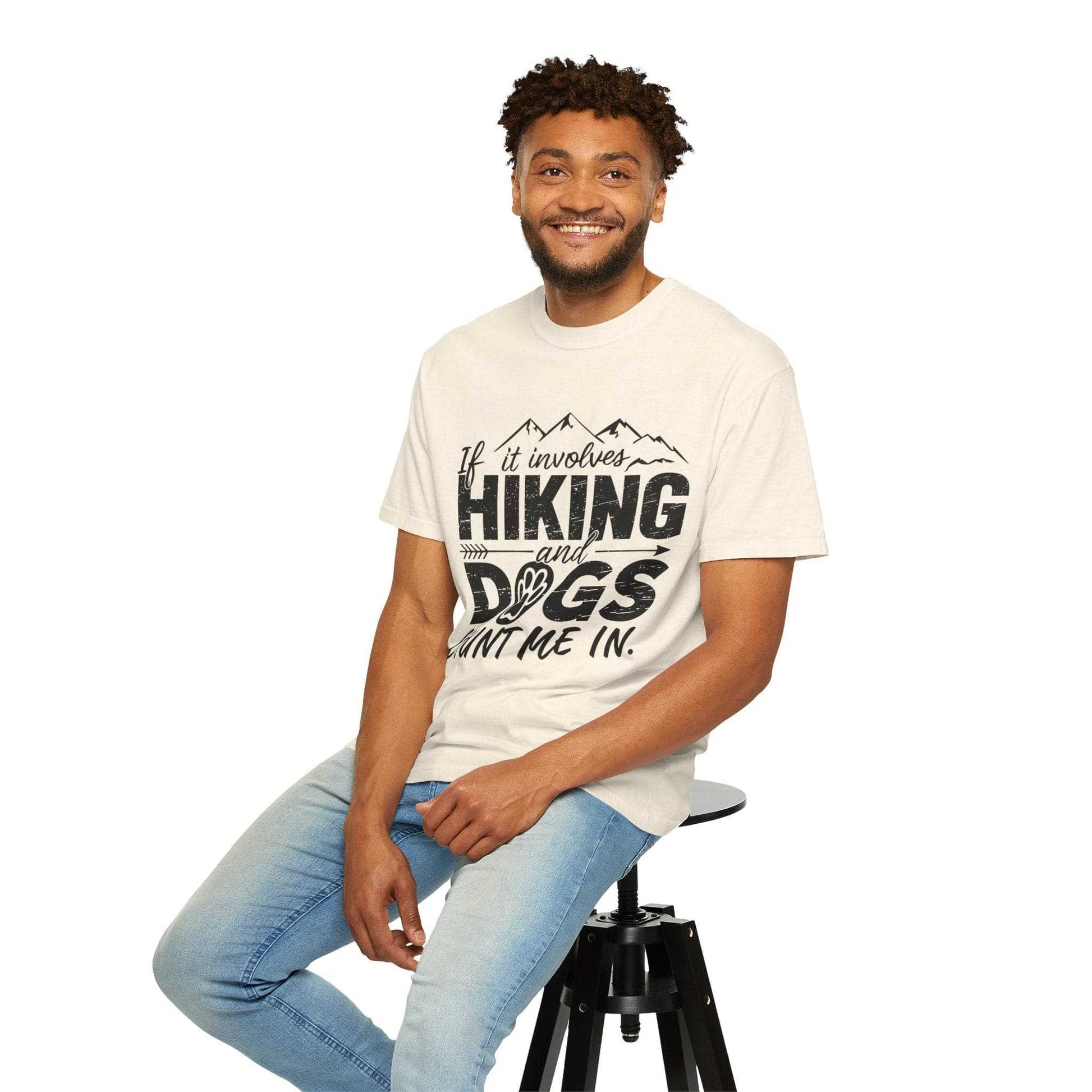 Man wearing a t-shirt with 'Hiking and Dogs' text, sitting on a stool against a white background