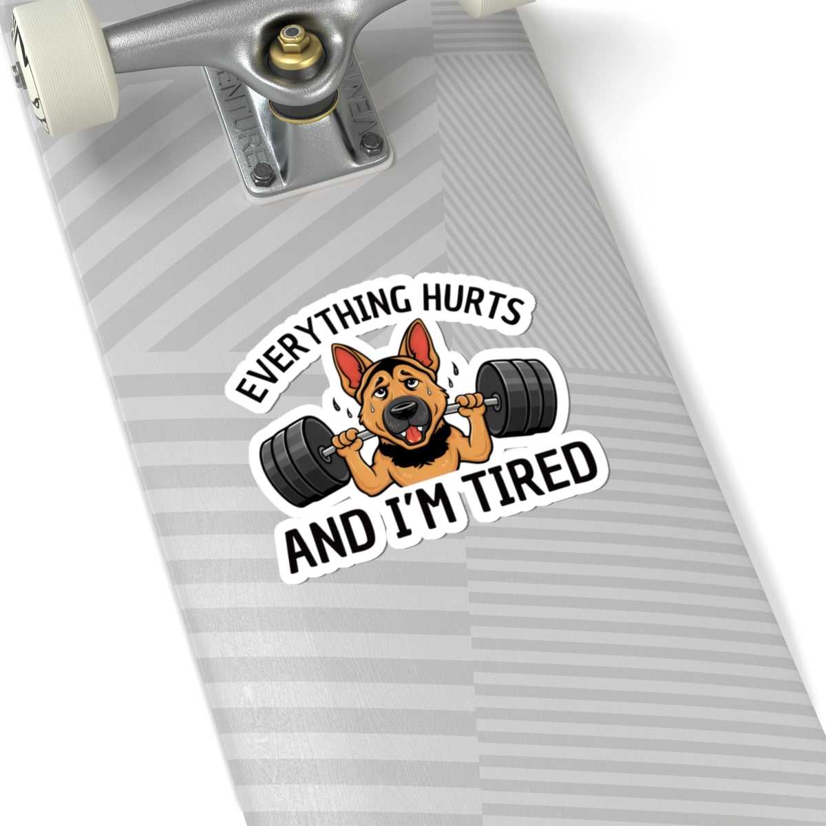 Skateboard with a sticker of a dog lifting weights and text 'Everything hurts and I'm tired' on a white background.