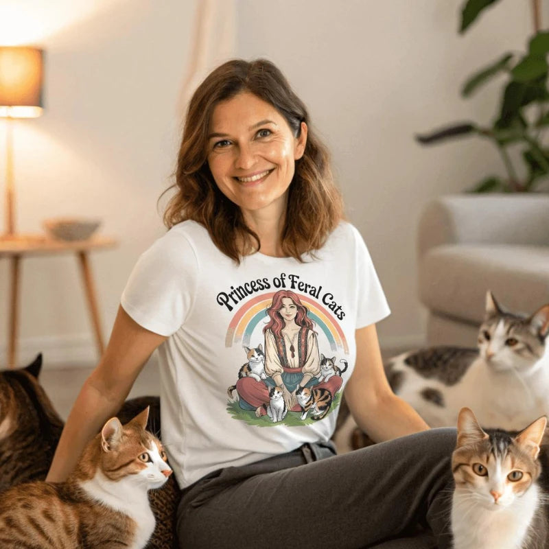 Woman wearing a 'Princess of Feral Cats' t-shirt surrounded by cats in a cozy room.