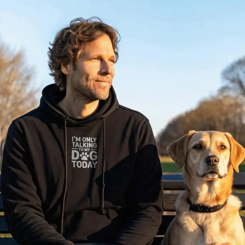 Man wearing a hoodie with text sitting next to a dog outdoors